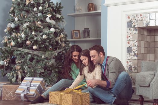 Happy family gather near Christmas tree with presents