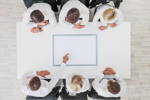 Business, people and team work concept - close up of creative team sitting at table and pointing finger to blank copy space for text