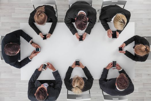 Top view of business people sitting around the table and using smartphones with blank screen