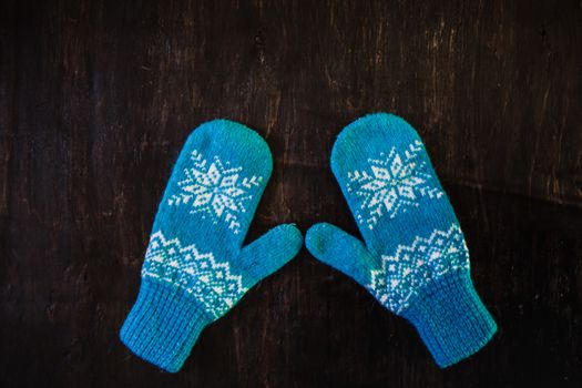 a pair of blue knitted mittens on a dark blue-green-brown wooden vintage background, copy space.