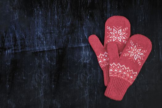 a pair of red-pink-lilac-magenta purple knitted mittens on a dark blue-green-brown wooden vintage background, copy space.