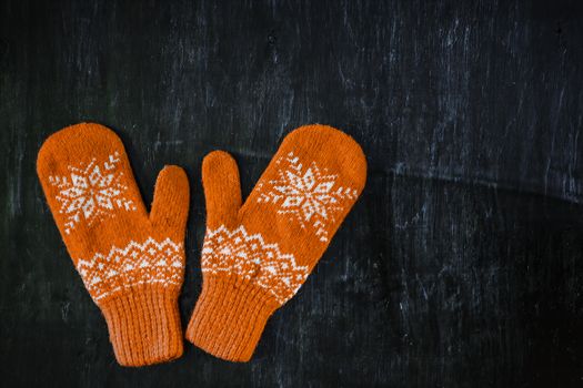 a pair of yellow orange knitted mittens on a dark blue-green-brown wooden vintage background, copy space.