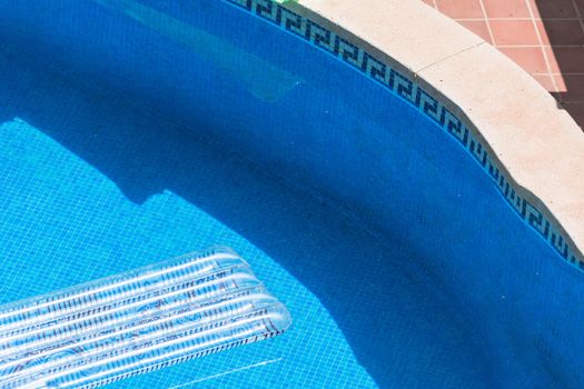 Transparent air mattress floats in a blue swimming pool.
