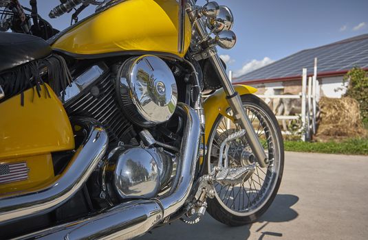 Customized yellow-colored motorcycle with chrome-plated parkings in a countryside landscape during an outdoor voyage.