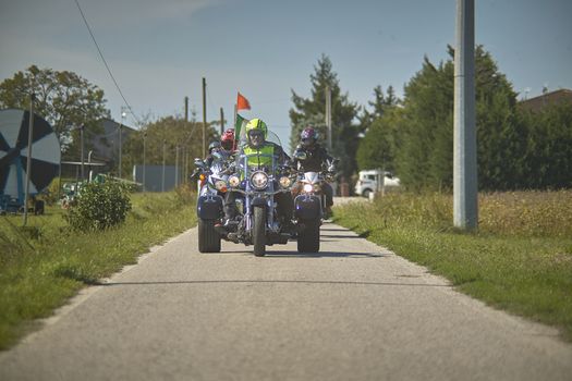 Front view of a trike on the road that comes to the shooting point, accompanied by a team of motorcyclists.