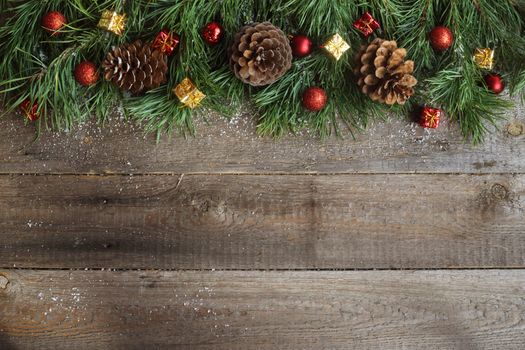 Christmas card on wooden background with snow fir tree, pine cones and decorative baubles. View with copy space