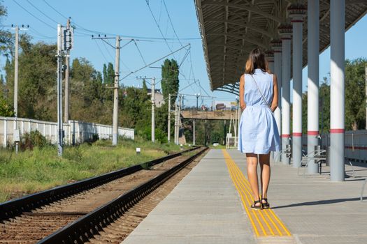 Young beautiful girl stands alone on a railway platform with her back to the camera