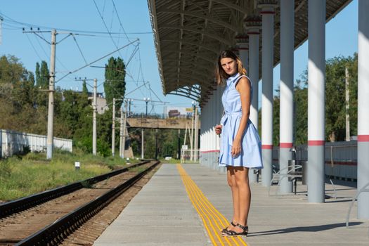 Young beautiful girl stands alone on a railway platform and looks into the distance with anticipation