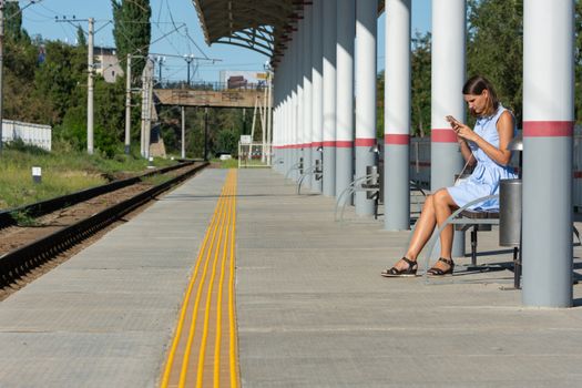 Young girl with a phone waits for a train on the empty platform of the railway station