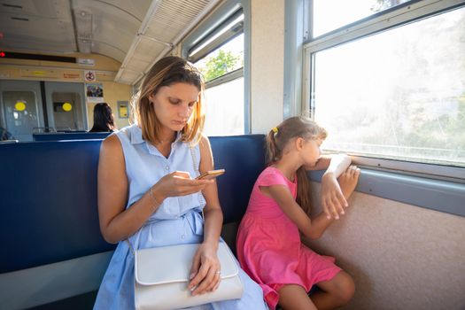 A young girl looks at the phone, daughter at the window in the electric train