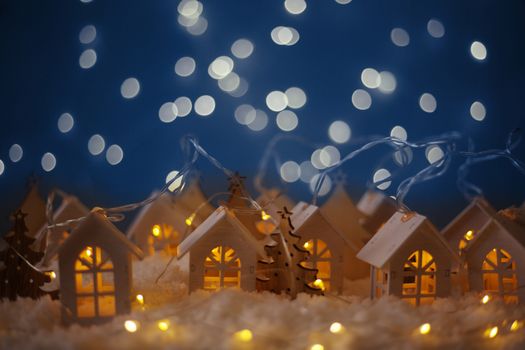 Christmas card of small glowing toy houses garland over bokeh lights background with copy space for text