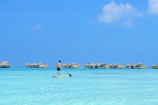 Young asian man paddle board rowing on sunny tropical paradise island with blue  sea water ocean in Maldives island.