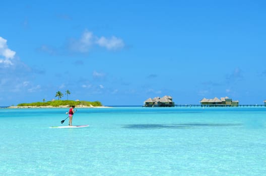 Young woman paddle board rowing on sunny tropical paradise island with blue sky sea water ocean in Maldives island.