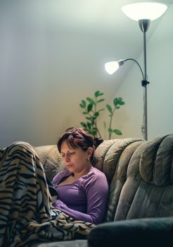 middle-aged woman is reading a book at home with the lamp on. Authentic photo, real people in real situation