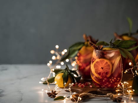 Winter sangria on dark christmas holiday background. Jugful of sangria and glasses with fruit slice, cranberry and rosemary. Copy space for text or design. Horizontal. Decoration lighting chain.