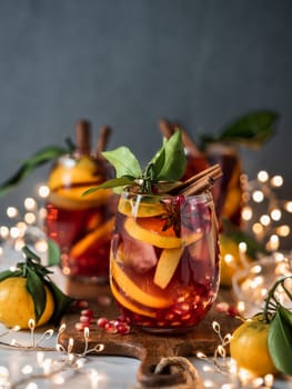 Winter sangria on dark christmas holiday background. Jugful of sangria and glasses with fruit slice, pomegranate and spices. Copy space for text or design. Vertical.