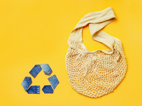 Reuse, reduce, recycle concept background. Recycle symbol made from old jeans and mesh bag on yellow background. Top view or flat lay. Copy space for text or design