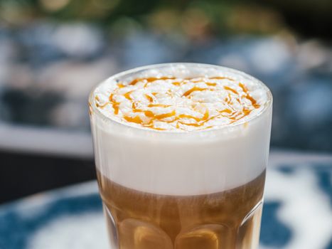 Hot latte macchiato coffee with caramel on tabletop outdoors. Natural hard daylight. Soft focus with bokeh. Close up view.