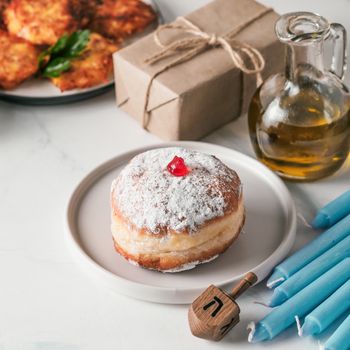 Jewish holiday Hanukkah concept and background. Hanukkah food doughnuts and potatoes pancakes latkes, oil, giftbox, candle and traditional spinnig dreidl on blue background. Copy space for text.
