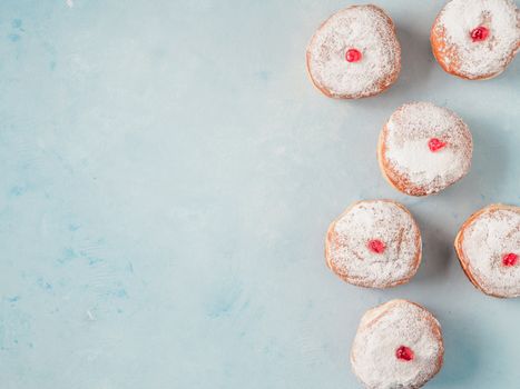 Hanukkah food doughnuts with jelly and sugar powder on blue background. Jewish holiday Hanukkah concept and background. Copy space for text. Top view or flat lay.