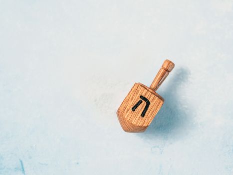Jewish holiday Hanukkah concept and background. Hanukkah traditional spinnig dreidl or dredel on blue background. Dreidel with letter He of Hebrew alphabet. Copy space for text. Top view or flat lay.
