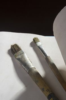 Old paint brushes and sheet of paper on a black background