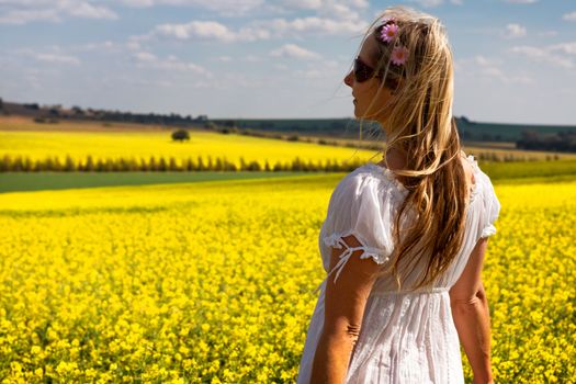 Woman in white cotton dress standing by a field of flowering golden canola on a beautiful spring day in the sunshine