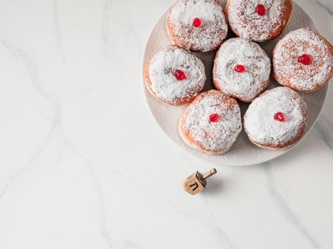 Jewish holiday Hanukkah concept and background. Hanukkah food doughnuts and traditional spinnig dreidl or dredel on white marble table background. Copy space for text. Shallow DOF.Top view or flat lay