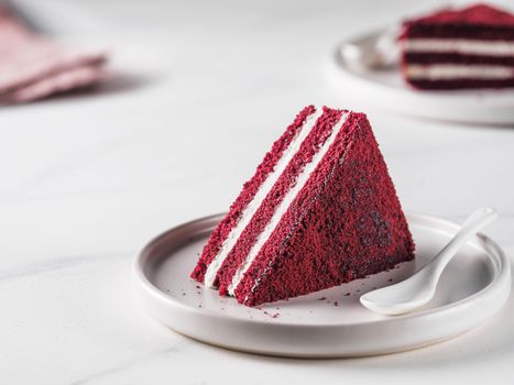 Piece of red velvet cake with perfect texture in matte plate on white marble tabletop. Slice of delicious homemade red velvet cake with raspberry and chocolate. Copy space for text.