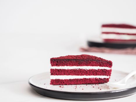 Piece of red velvet cake with perfect texture in matte plate on white marble tabletop. Slice of delicious homemade red velvet cake with raspberry and chocolate. Copy space for text.