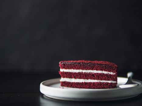 Piece of red velvet cake with perfect texture in matte plate on black tabletop. Slice of delicious homemade red velvet cake with raspberry and chocolate. Copy space for text.