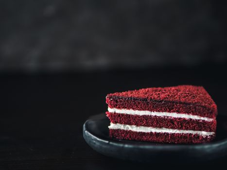 Piece of red velvet cake with perfect texture in matte plate on black tabletop. Slice of delicious homemade red velvet cake with raspberry and chocolate. Copy space for text.