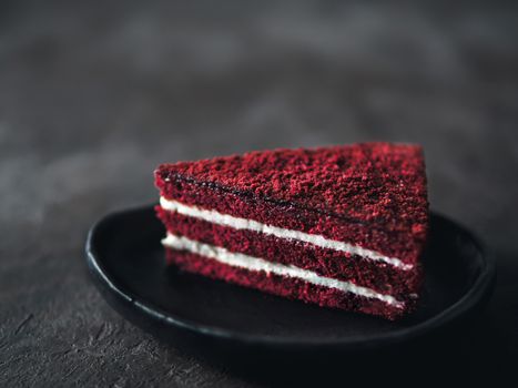 Piece of red velvet cake with perfect texture in matte plate on black tabletop. Slice of delicious homemade red velvet cake with raspberry and chocolate. Copy space for text.