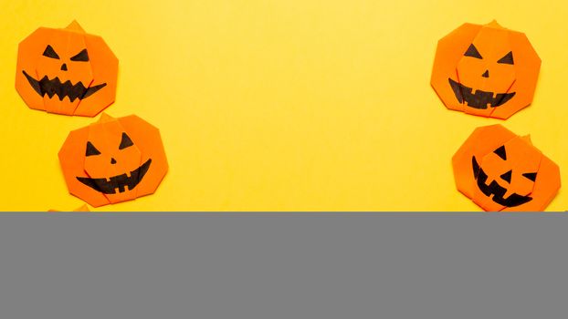 Halloween concept. Paper origami pumpkin on yellow background. Simple idea for halloween - easy made paper pumpkins on trendy color Ceylon Yellow background. Copy space for text. Banner
