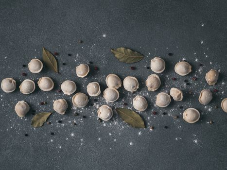 Pattern of frozen uncooked russian pelmeni with peppercorns and bay leaves on black background. Creative layout of dumplings. Beautiful scattered raw dumplings. Top view or flat lay.