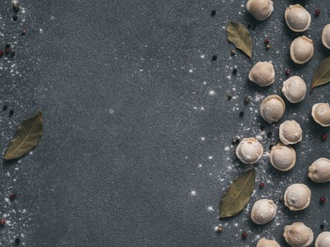Pattern of frozen uncooked russian pelmeni with peppercorns and bay leaves on black background. Creative layout of dumplings. Beautiful scattered raw dumplings. Top view, flat lay. Copy space for text