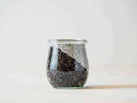 Healthy breakfast concept and idea - two colors chia pudding on white tabletop. Glass jar with black charcoal and white vegan milk chia pudding. Copy space for text