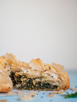 Greek pie spanakopita on blue table with shallow DOF. Slice of vegetarian or vegan Spanakopita Spinach Pie with copy space. Vertical. Ideas and recipes for healthy lunch.