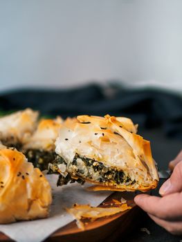 Slice of greek pie spanakopita in hand. Ideas and recipes for vegetarian or vegan Spanakopita Spinach Pie from fillo pastry cut in slices. Copy space. Side view. Vertical.