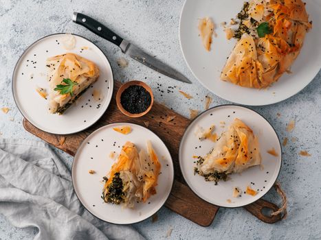 Greek pie spanakopita on gray background. Ideas and recipes for vegetarian or vegan Spanakopita Spinach Pie from fillo pastry. Slices pie on plates. Copy space. Top view or flat lay.