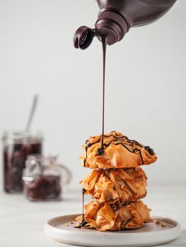 Ideas and recipes for sweet baking. Fillonuts - peanut butter and jelly fillo doughnuts pouring chocolate syrup. On white marble table. Copy space for text. Vertical.