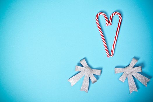 Christmas or winter composition. Heart shaped candy canes with two glittery silver bows on pastel blue background. Christmas, winter, new year concept. Flat lay, top view, copy space.