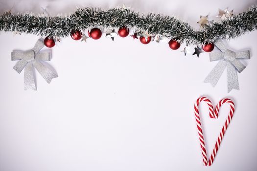 Christmas composition. Garland with red balls, stars, glittery bows and heart made of candy canes on white background. Christmas, winter, new year concept. Flat lay, top view, copy space.