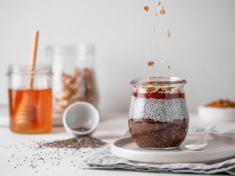 Healthy breakfast concept and idea- chia pudding with organic raw cocoa, berries jam and oatmeal granola.Glass jar with chocolate chia pudding with falling oatmeal on white table.Copy space