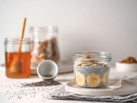 Healthy breakfast concept and idea - chia pudding with organic banana and bee pollen. Glass jar chia puding on white marble table. Copy space for text