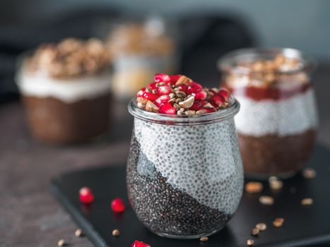 Healthy breakfast concept and idea - two colors chia pudding with organic raw pomegranate, almond and hemp grains. Glass jar with black charcoal and white vegan milk chia pudding. Copy space for text