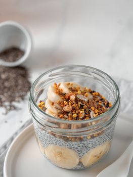 Healthy breakfast concept and idea - chia pudding with organic banana and bee pollen. Glass jar chia puding on white marble table. Copy space for text
