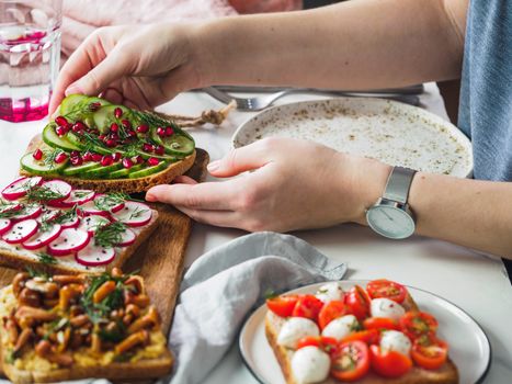 Female hands on dinning table. Young woman eat vegetarian toast. Vegan veggies sandwiches on dinning table