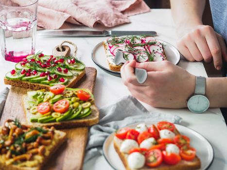 Female hands on dinning table. Young woman eat vegetarian toast. Vegan veggies sandwiches on dinning table