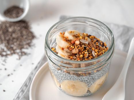 Healthy breakfast concept and idea - chia pudding with organic banana and bee pollen. Glass jar chia puding on white marble table. Copy space for text
